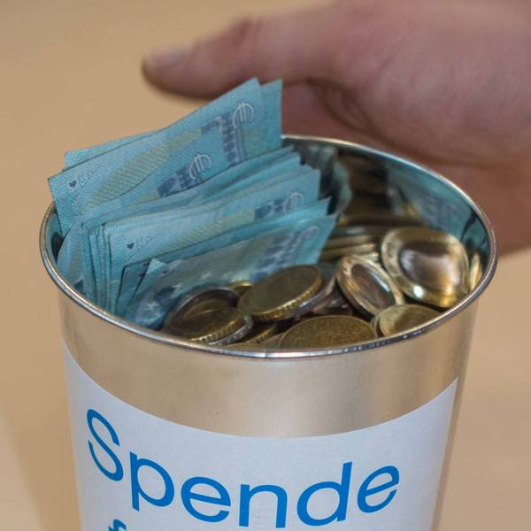 Eine offene Spendendose mit Münzen und Scheinen. Die Dose trägt den Schriftzug
